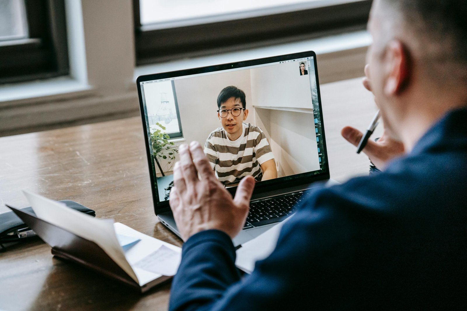 Two professionals engaged in an online video conference on a laptop in an indoor setting.